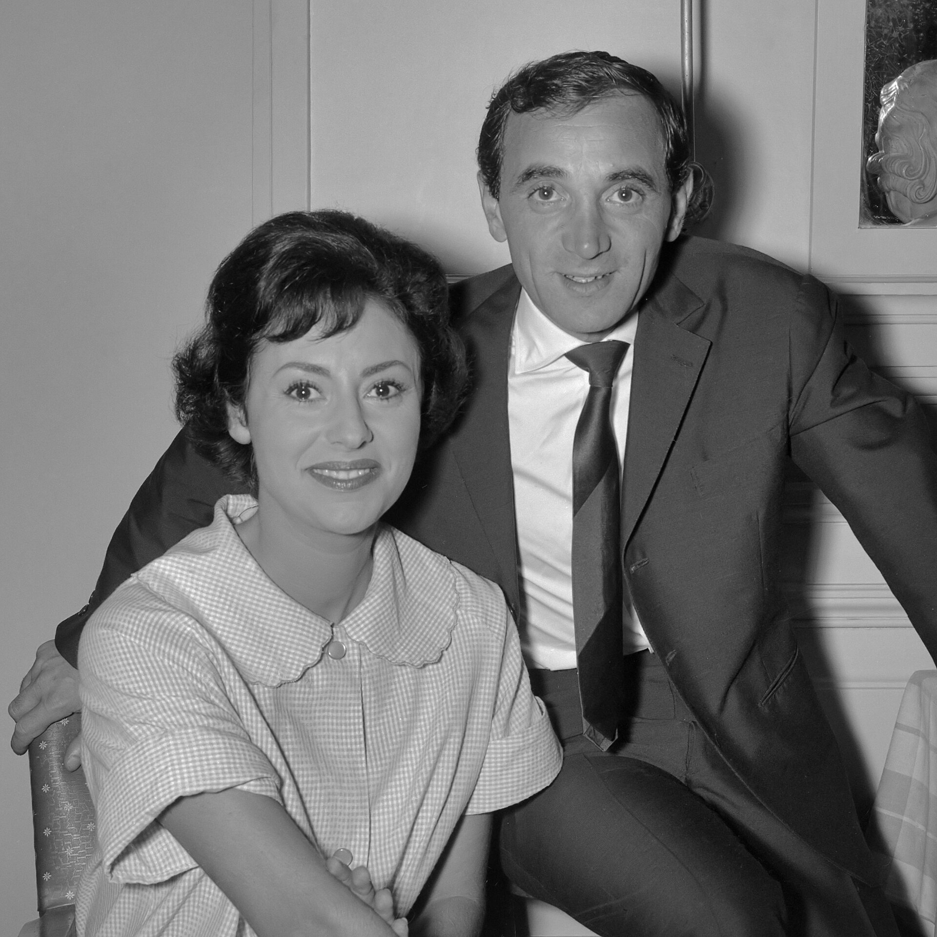 Aznavour in a suit leaning over a seated woman backstage, 1961