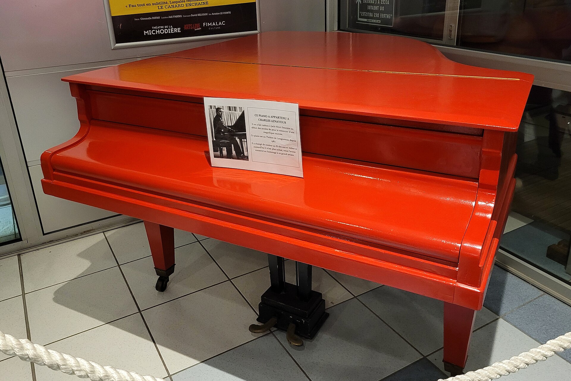 A piano in a museum display case, labelled as belonging to Aznavour's teacher Jack-Henri Soutter